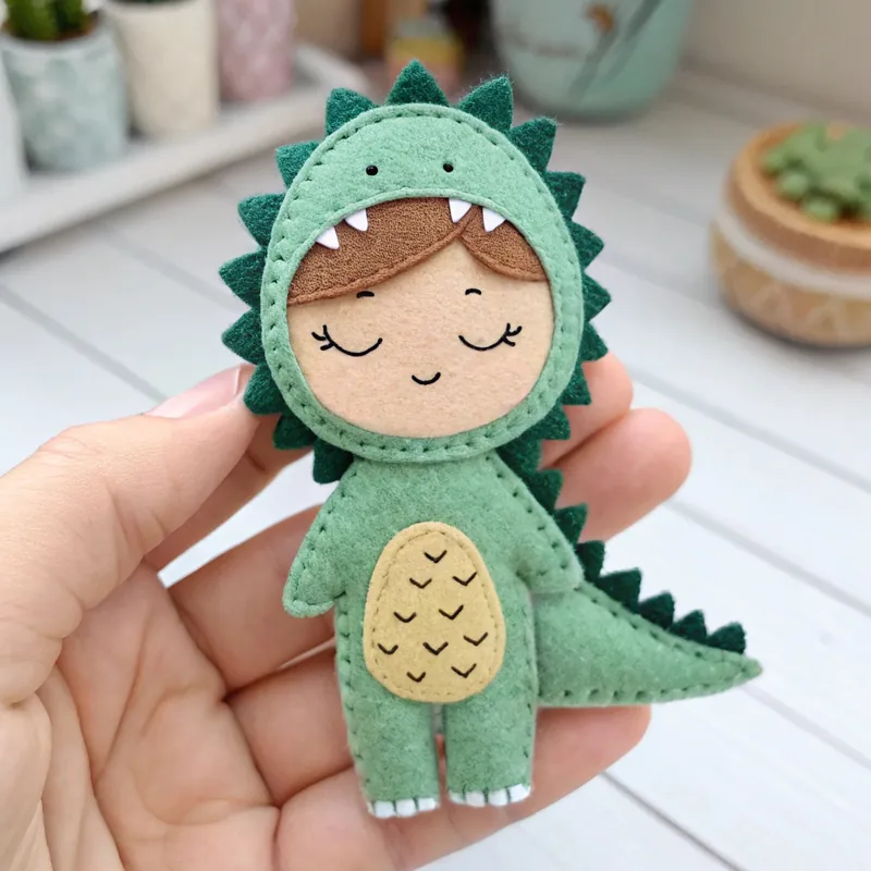 Finished felt boy doll asleep in a green dinosaur onesie with spikes and a tail