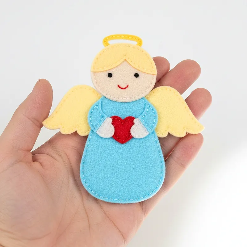 Finished felt angel ornament in a blue dress with golden wings and a halo, holding a red heart