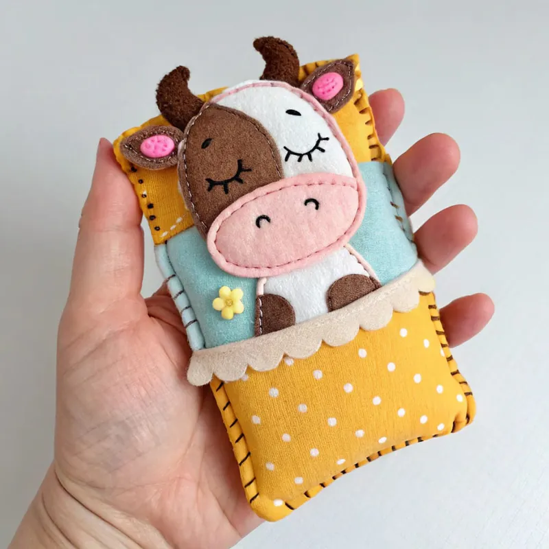 Finished sleeping felt cow tucked under a yellow polka-dot quilt on a mint blanket