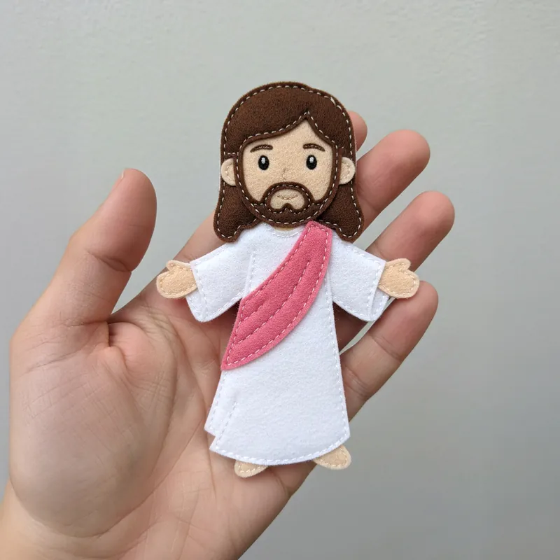 Finished felt figure of Jesus in a white robe with a pink sash and open arms