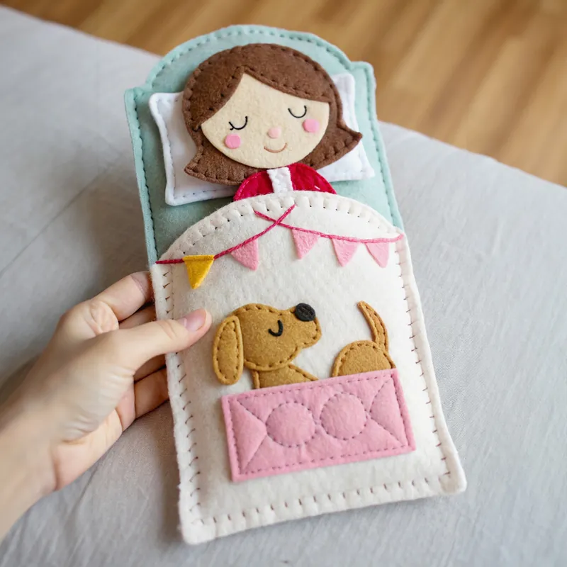 Finished felt bedtime scene of a girl asleep in a mint bed with a puppy and pink bunting